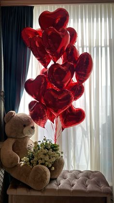 a teddy bear sitting on top of a bench next to some balloons in the shape of hearts