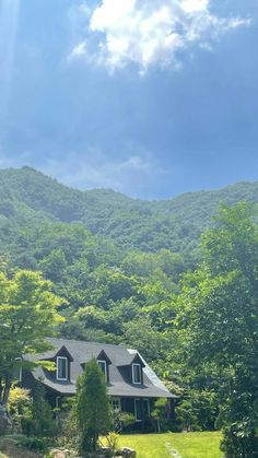 the house is surrounded by lush green trees and mountains in the distance, with blue skies overhead