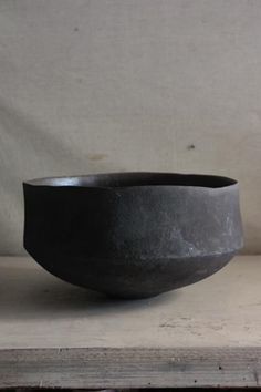 a large black bowl sitting on top of a wooden table next to a white wall