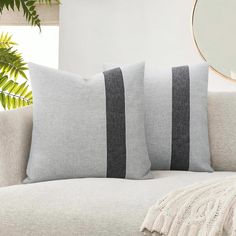 two grey and black striped pillows on a white couch with a mirror in the background