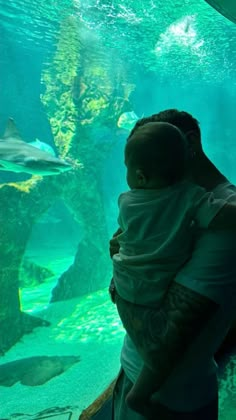 a man holding a baby in his arms looking at fish inside an aquarium tank with green water