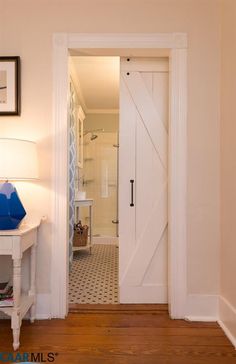 an open door leading to a bedroom with a white table and lamp on the side