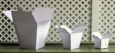 three white vases sitting on top of a green table next to a wallpaper