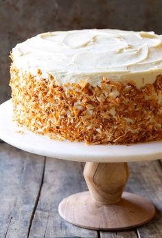 a carrot cake with white frosting and toasted coconut flakes on a wooden stand