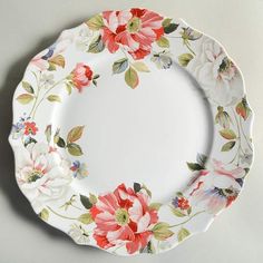 a white plate with red and pink flowers painted on the side, sitting on a table