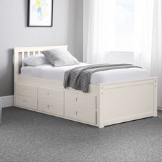 a white bed with drawers underneath it in a room next to a window and rug on the floor