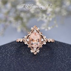 a ring with an oval cut peach morganite surrounded by small white diamonds on a black surface