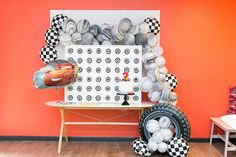 an assortment of balloons and race cars are displayed on a table in front of a red wall