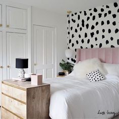 a bedroom with black and white wallpaper, pink headboard, and wooden dresser