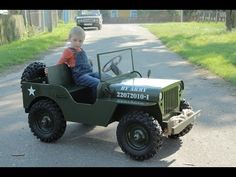 a little boy riding on the back of a green jeep