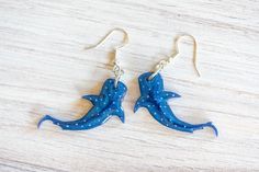 two blue dolphins are hanging from gold earwires on a wooden surface with white dots