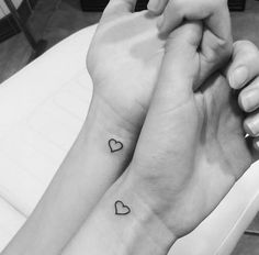 two people holding hands with small hearts on their wrist tattooing each other's wrists