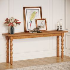 a wooden table topped with a vase filled with flowers next to a framed bird on top of it