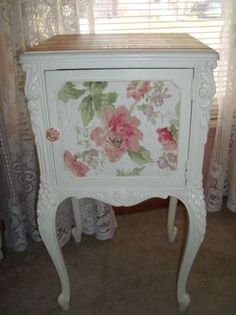 a white cabinet with pink flowers painted on the front and side panels, sitting next to a window