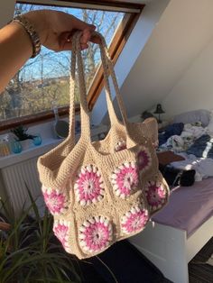 a hand holding a crocheted purse in front of a bed with a window