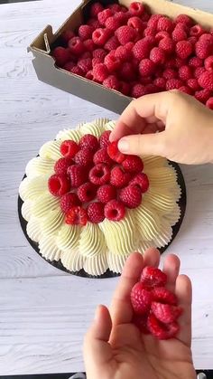 two hands reaching for raspberries on top of a cake in the shape of a flower