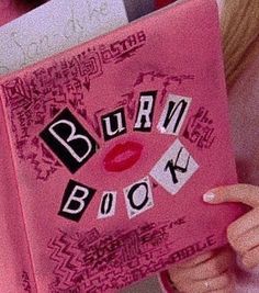 a woman holding up a pink book with the words burn book written on it