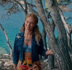 a woman standing next to some trees near the water