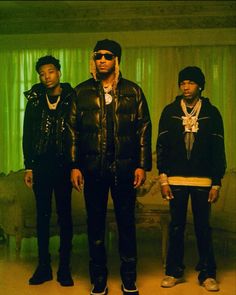 three young men standing next to each other in front of a green curtained room