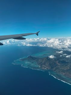 an airplane wing flying over the ocean and land near some clouds in the blue sky