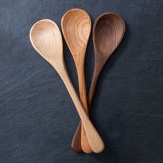 three wooden spoons sitting next to each other on a black surface with dark background