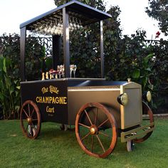 an old fashioned cart with wine glasses on top is sitting in the grass near some bushes