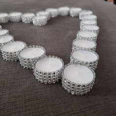 several white candles are arranged in the shape of a heart on a gray tablecloth