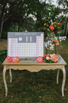 a table with flowers on it and a calendar sitting on top of it in front of some trees