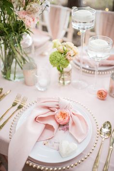 the table is set with pink napkins, silverware and flowers in vases