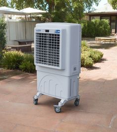 a white air cooler sitting on top of a brick floor next to a park bench