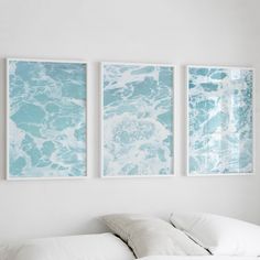 three paintings hang on the wall above a bed in a white room with pillows and blankets