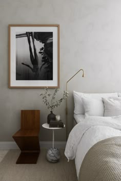 a bed with white sheets and pillows in a room next to a table, lamp and pictures on the wall