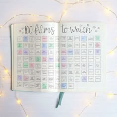 an open planner with the words 100 films to watch written on it and lights in the background