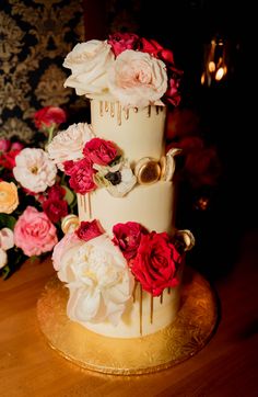 a three tiered wedding cake with flowers on the side and gold trimmings