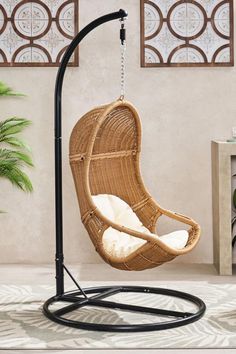 a rattan swing chair hanging from a black metal stand with white cushions on it