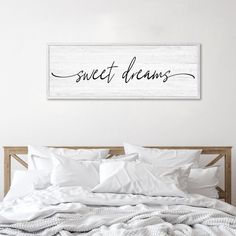 a bed with white sheets and pillows under a sign that says sweet dreams on it