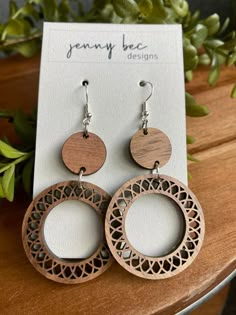 wooden earrings with laser cut designs on them sitting on a table next to a plant