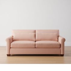 a pink couch sitting on top of a hard wood floor next to a white wall