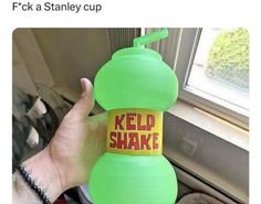 a person holding up a green bottle with the words red shake on it and an orange sticker that says, f k a stanley cup