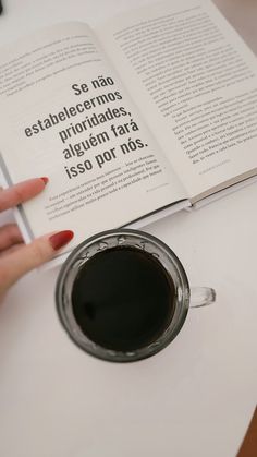 a woman is holding a book over a cup of coffee on a table with an open book in front of her