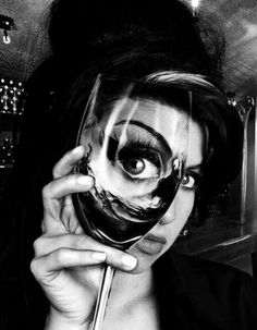 a woman holding a wine glass up to her face and looking through it with an eyeball in front of her