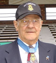 an older man wearing a hat and tie in front of some bleacher seats