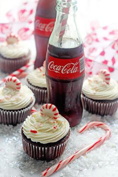 cupcakes with white frosting and candy canes next to coca - cola bottles