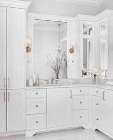 a bathroom with white cabinets and marble counter tops, gold accents on the mirror above the sink