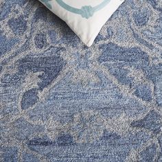 a blue and white pillow on top of a bed next to a wall with an ornate pattern