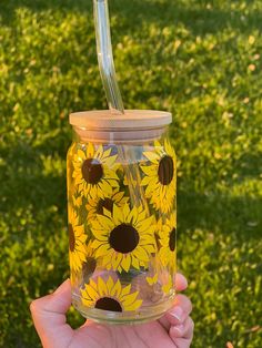 a hand holding a mason jar with sunflowers painted on it and a straw