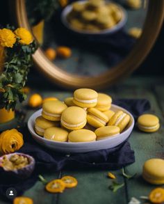 a plate full of yellow macaroons sitting on a table next to some flowers