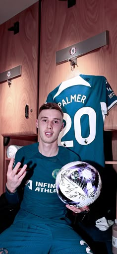 a man sitting in a locker holding a soccer ball and wearing a number 20 jersey