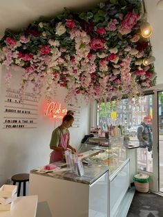 a woman standing in front of a counter with flowers hanging from it's ceiling