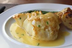 a white plate topped with meat and potatoes covered in gravy on top of a wooden table